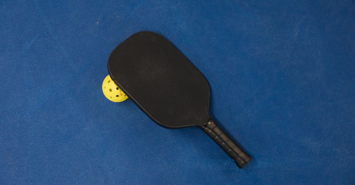 A pickleball paddle and ball on a textured blue surface, showcasing sports equipment.